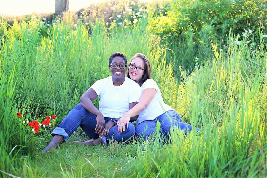 portrait of lesbian transracial couple sitting in a field with tall grass