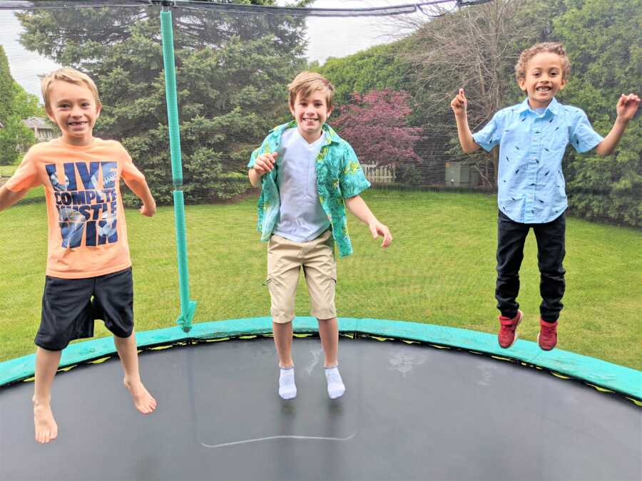 Three brothers smile while jumping on a trampoline together