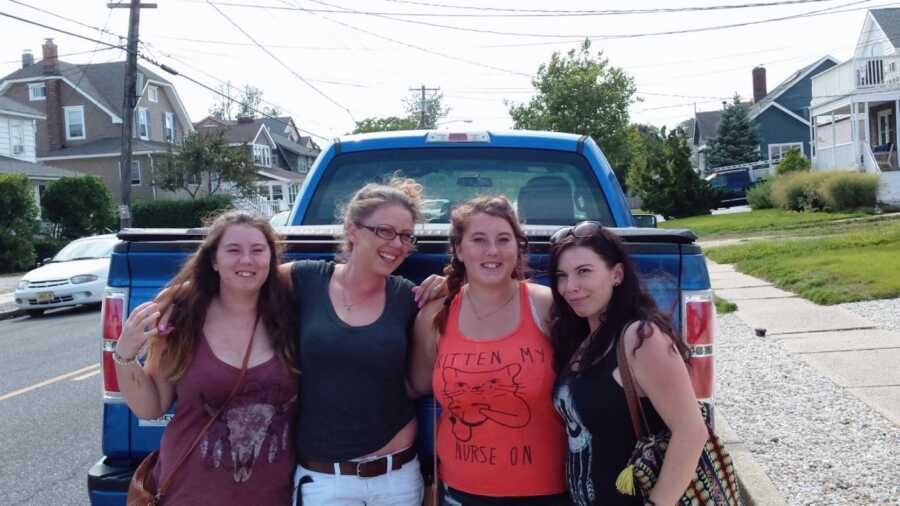 Four sisters take a group photo together while standing in front of a blue truck