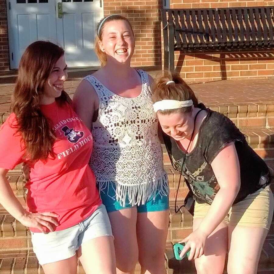 Three sisters laugh while taking photos together in their front yard