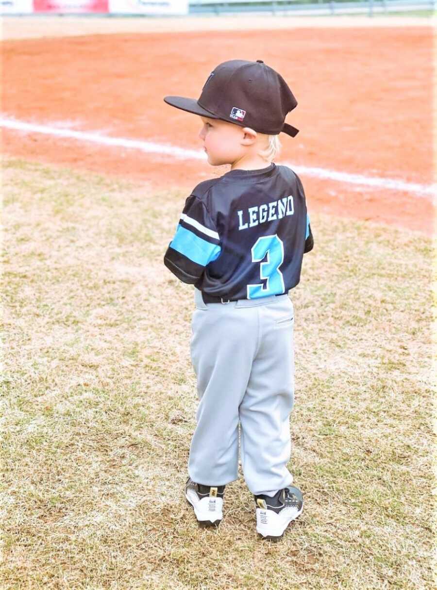 young baseball player standing on a baseball field with his name on the back of his shirt 