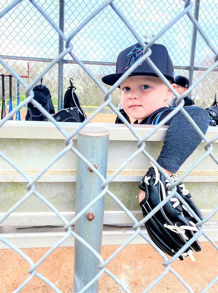 Young baseball player sitting on a bench chair wearing a baseball glove and hat