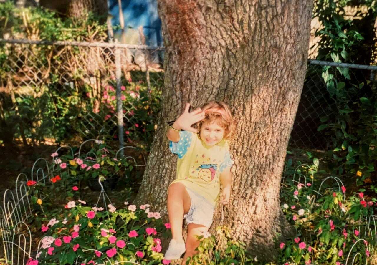 Little girl takes a funny photo next a tree, surrounded by pink flowers