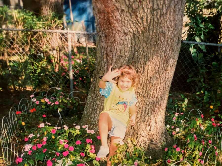 Little girl takes a funny photo next a tree, surrounded by pink flowers
