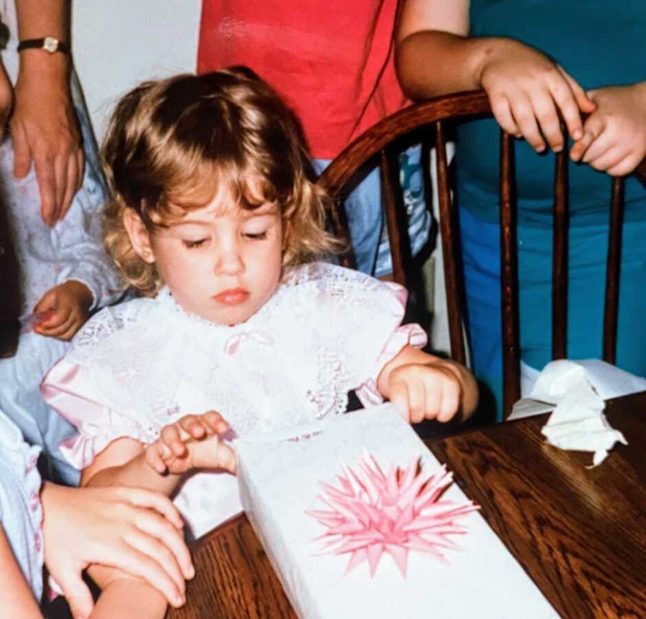 Little girl carefully unwraps a present on her birthday