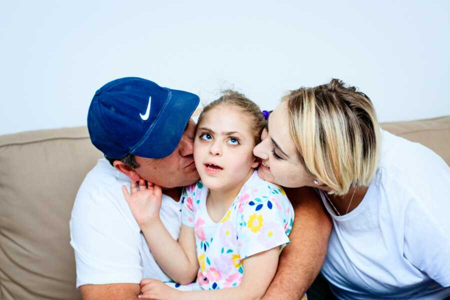 little girl kissed by both her parents