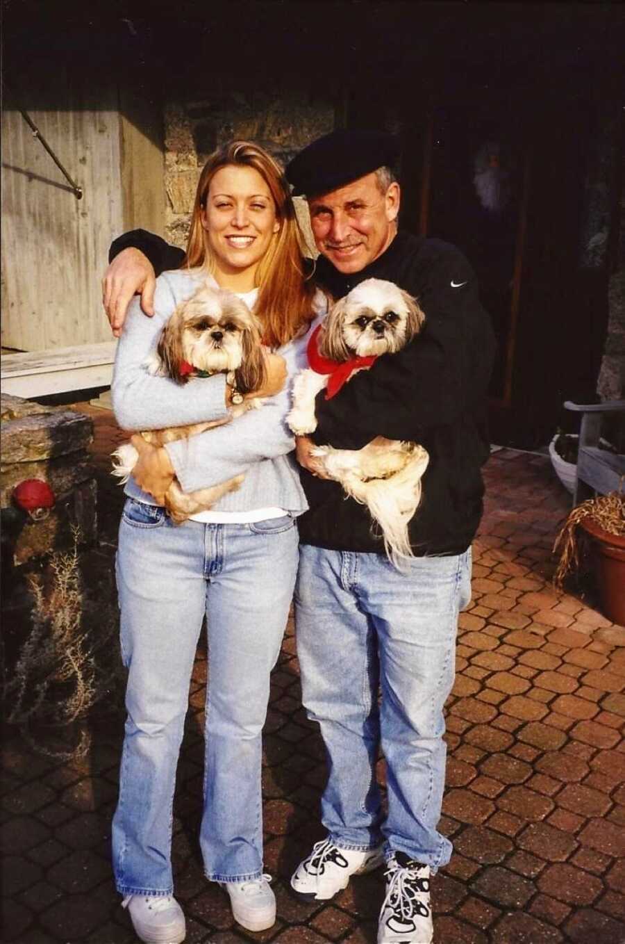 Father and daughter take a photo together, both wearing sweaters and jeans and holding dogs