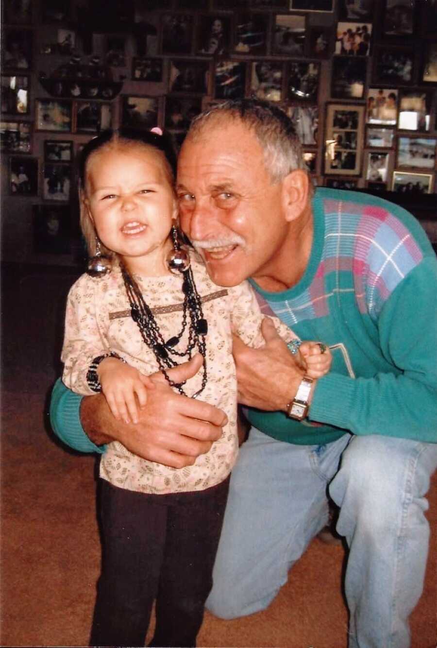 Grandpa smiles for a photo in a sweater with his granddaughter