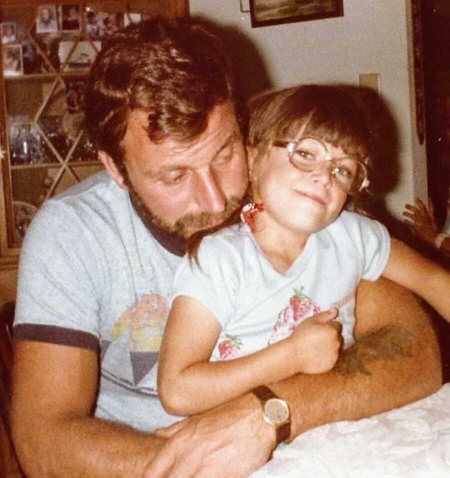 Little girl with glasses cuddles with her dad on the couch