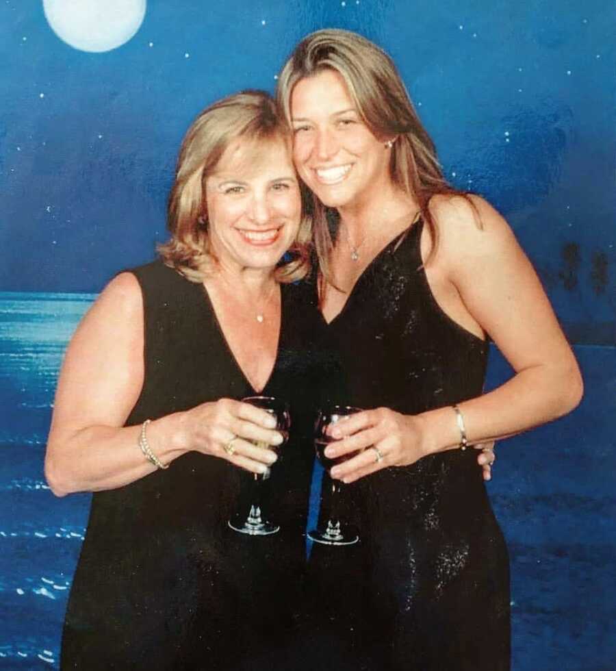 Mom and daughter pose for a photo on a cruise ship, both in black dresses and holding drinks