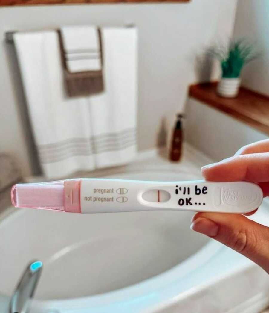 Woman takes a photo of a negative pregnancy test with "I'll be ok..." written on it