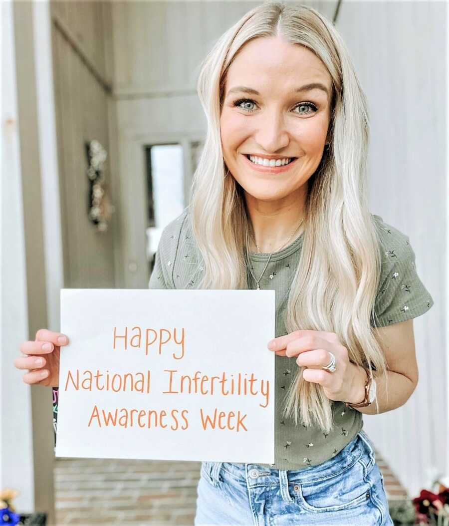 Young woman holding a handwritten sign that says "Happy National Infertility Awareness Week"
