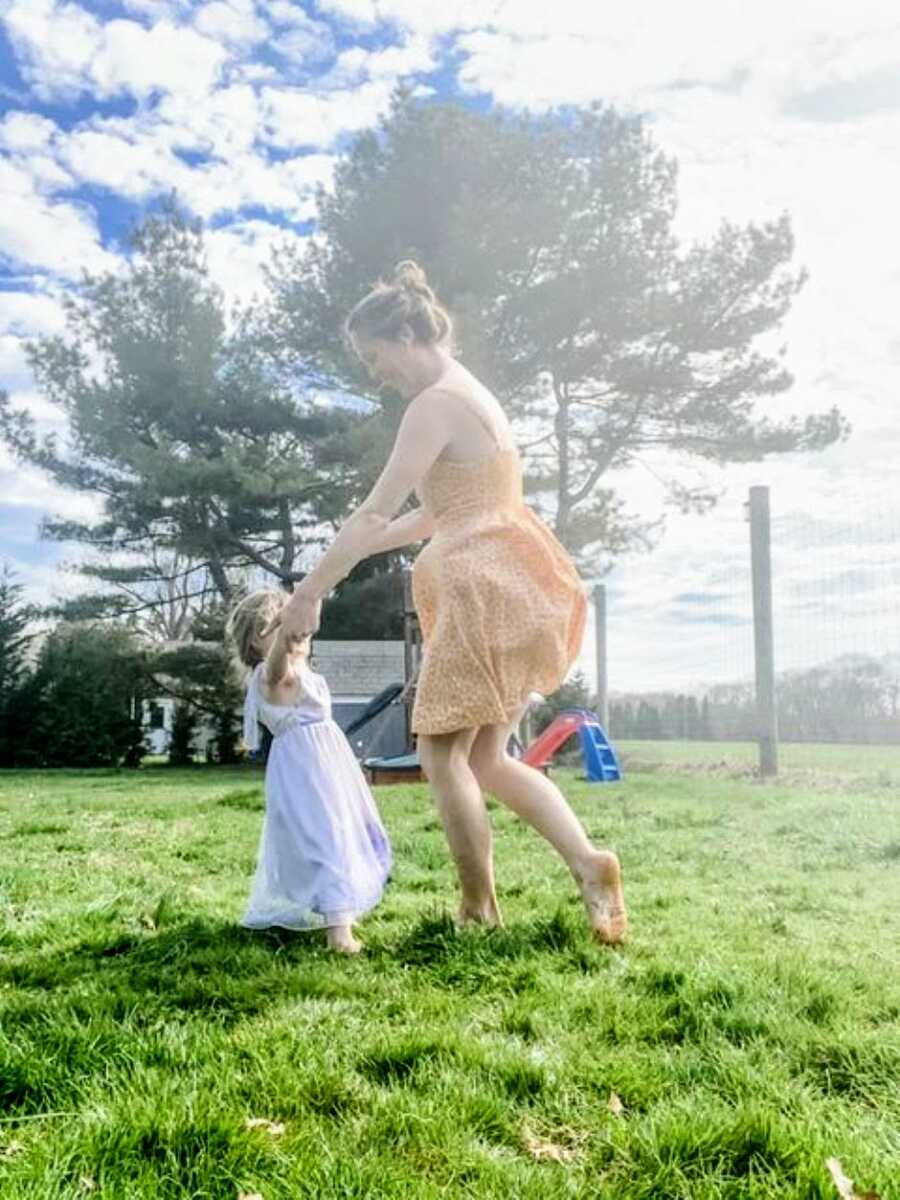 Mom and daughter dance barefoot in their backyard together