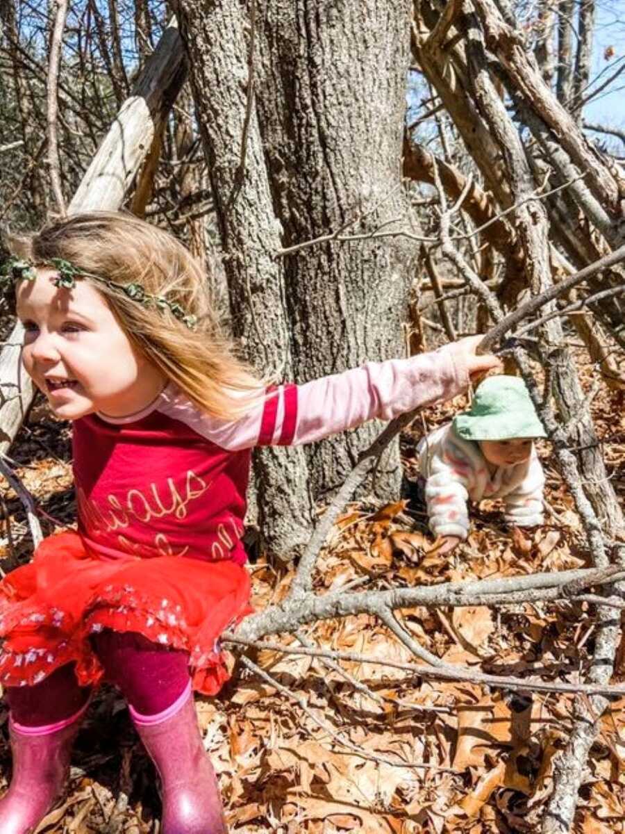 Two daughters crawl around in leaves during a family walk in the woods