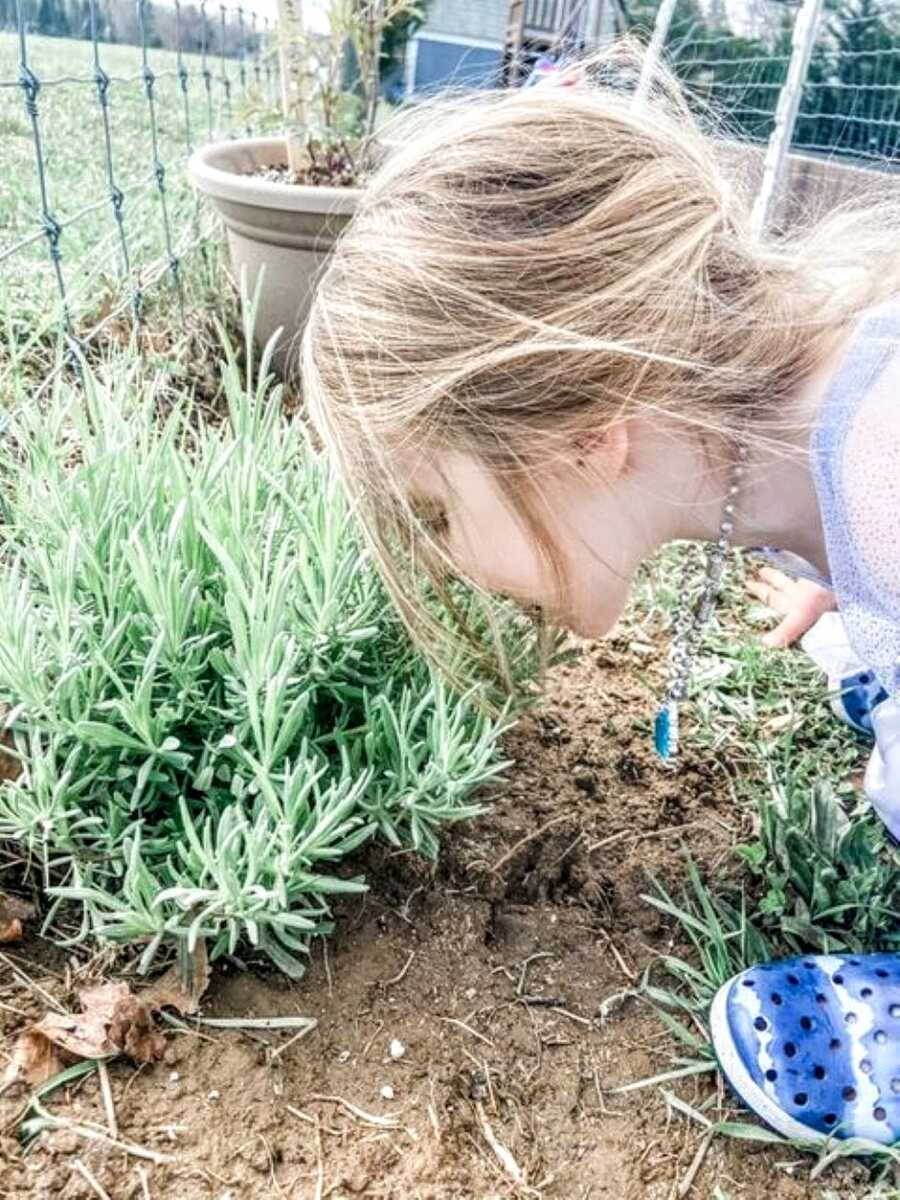 Little girl inspects a plant growing in her backyard