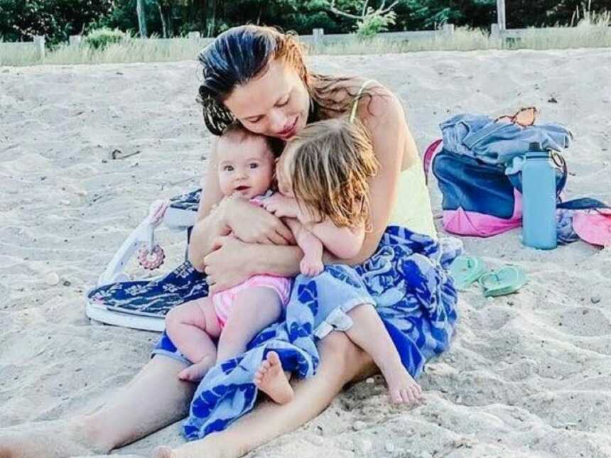 Woman clutches her two daughters while they dry off after swimming in the ocean at the beach