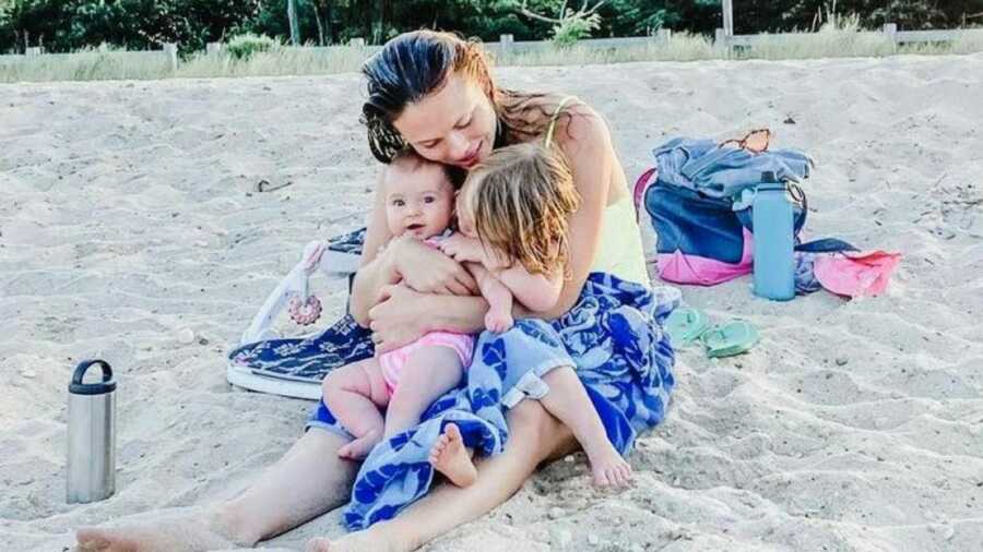 Woman clutches her two daughters while they dry off after swimming in the ocean at the beach