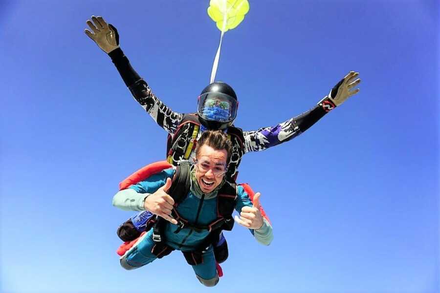 Young man skydiving with a professional assistant smiling and doing hand gestures 