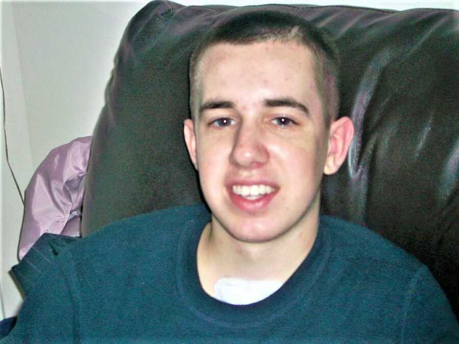 young man sitting on a couch with a pad on his chest and a scar on his head form a brain injury 