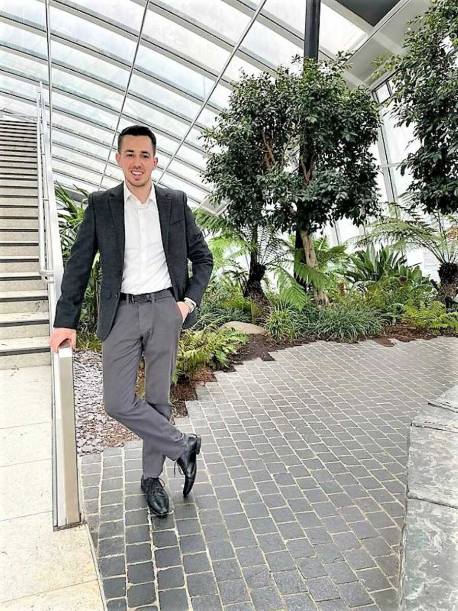 Young man wearing a semi-formal suit and standing next to stairs with trees in the background 