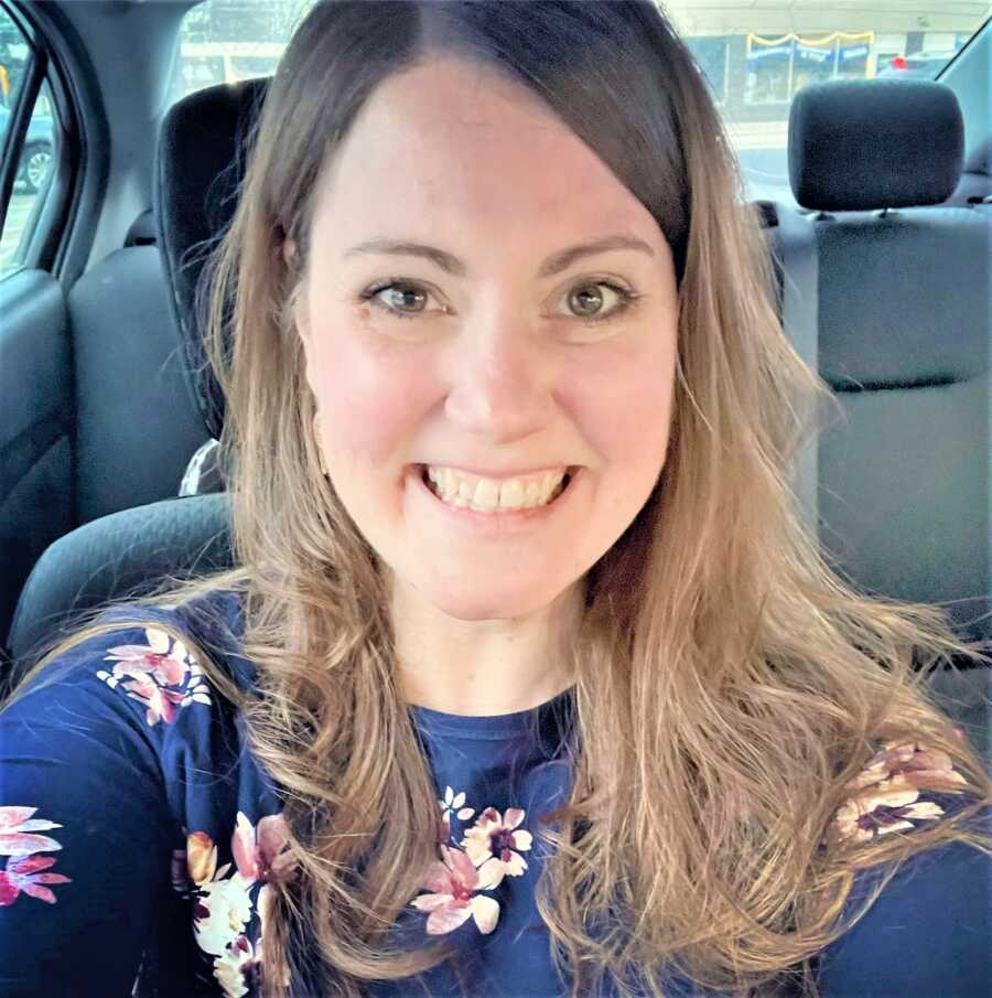 Selfie of woman in a car smiling wearing a navy blue shirt with floral print