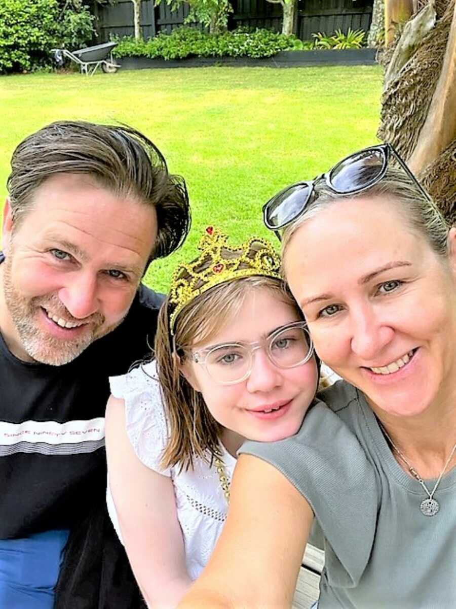 Parents take a selfie with their special needs daughter while she wears a crown