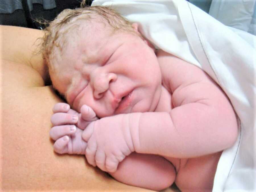 newborn baby girl resting of her other's naked chest right after birth 