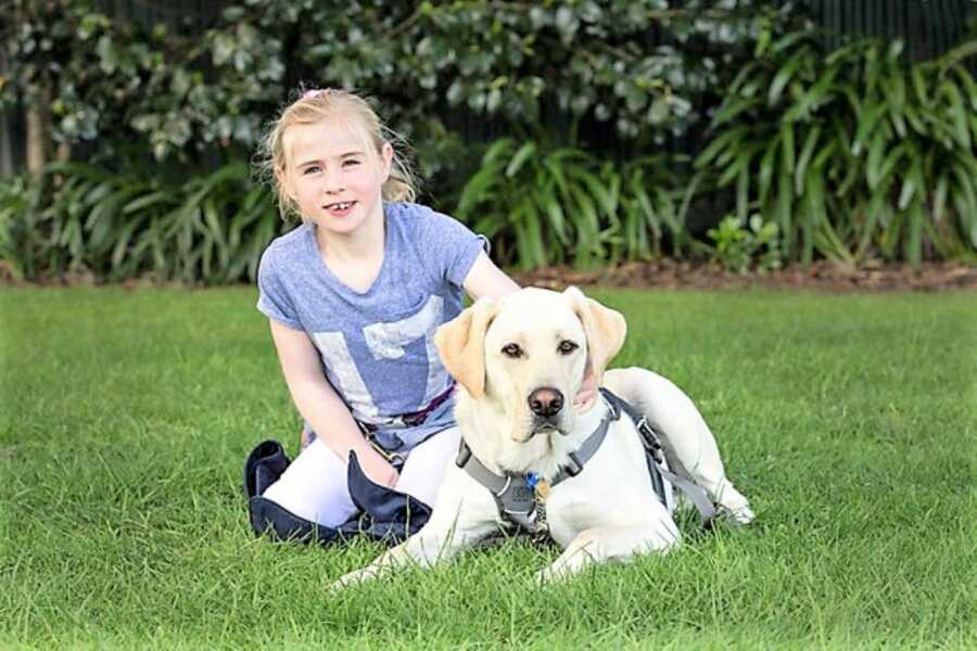 young girl sitting in the grass with her dog 