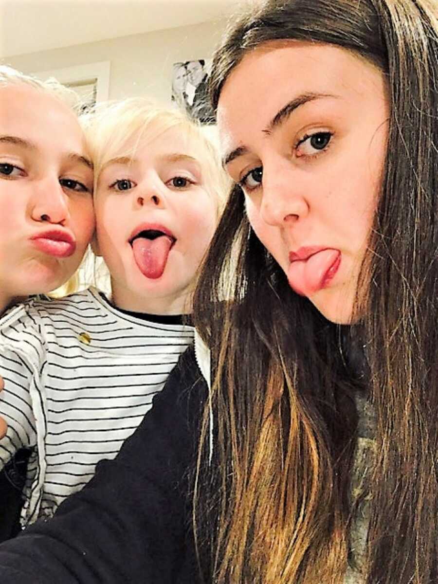 two older sisters and their toddler sister ticking their tongue out 
