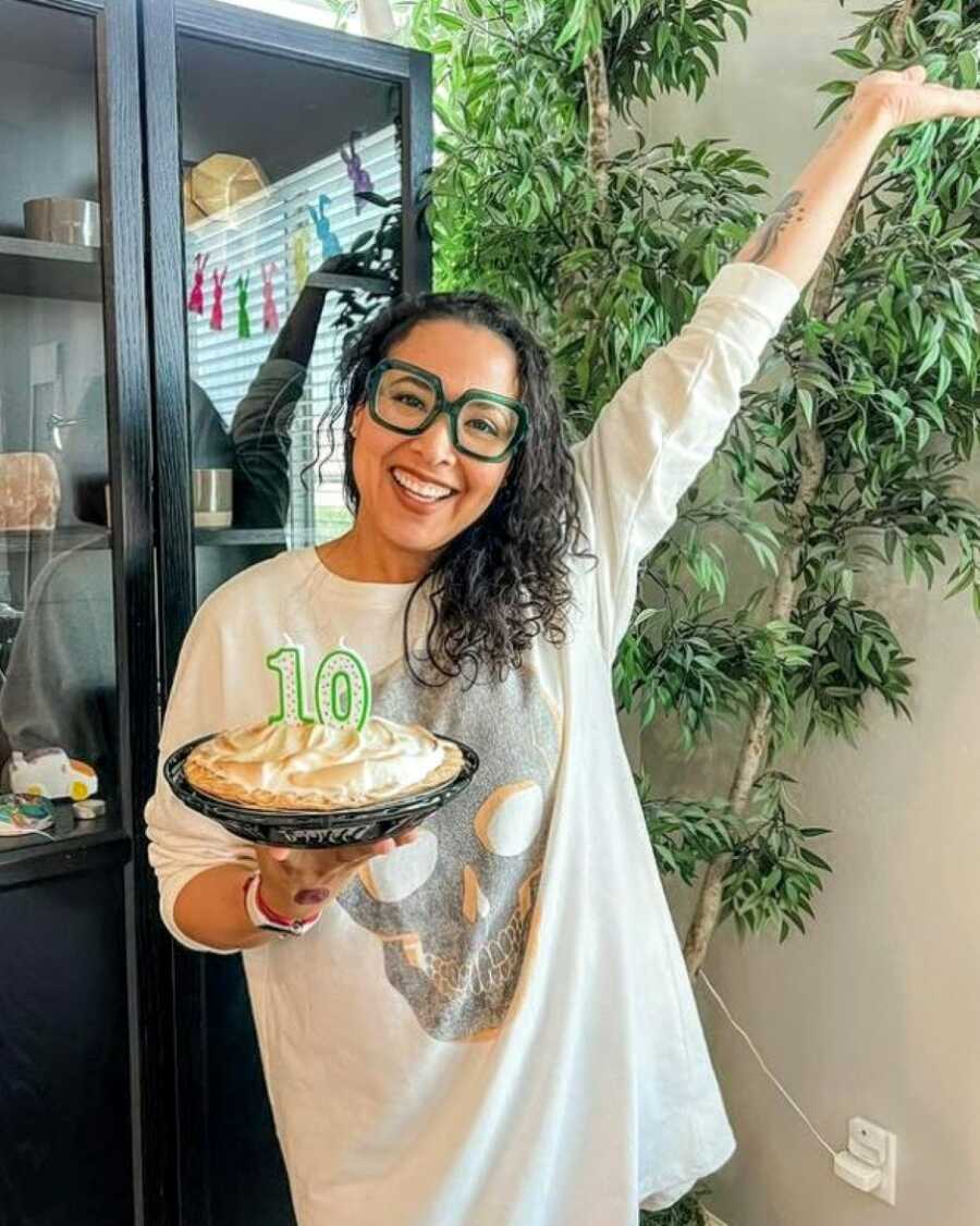 Woman celebrating 10 years of sobriety holds a pie with #10 candles in it