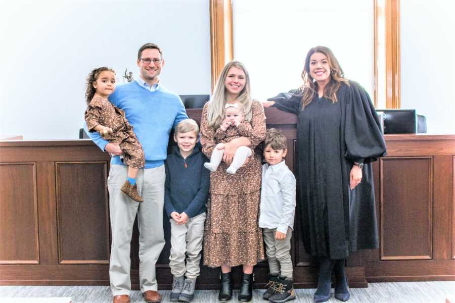 Mom dad and their 4 kids standing next to the judge at the courtroom 