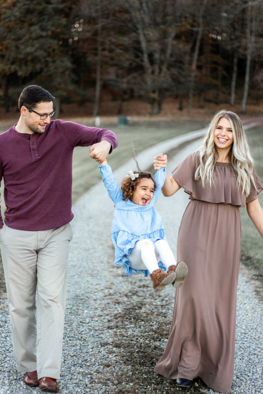 Mom and dad carrying their adoptive daughter by her arms while she looks happy and thrilled 