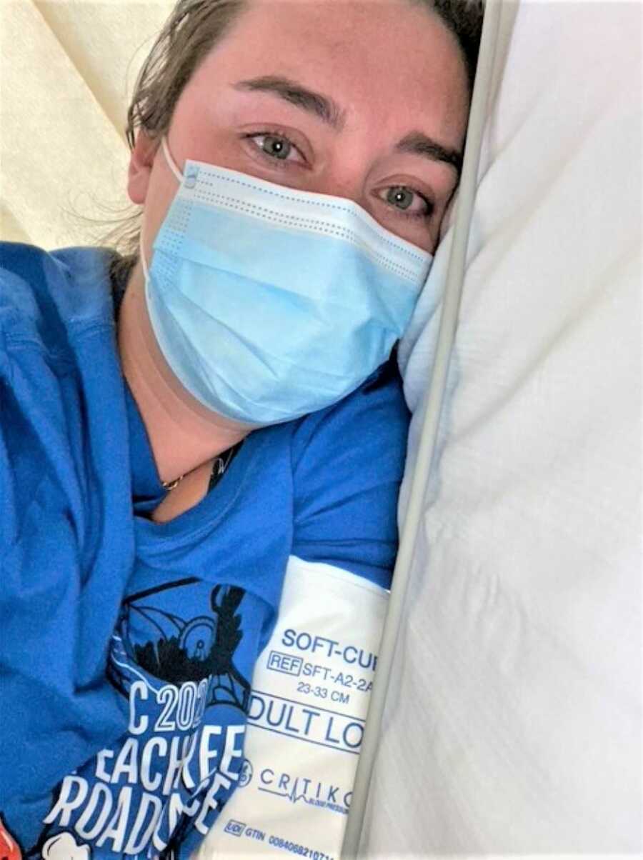 selfie of a woman at the hospital laying on bed with a blue mask on