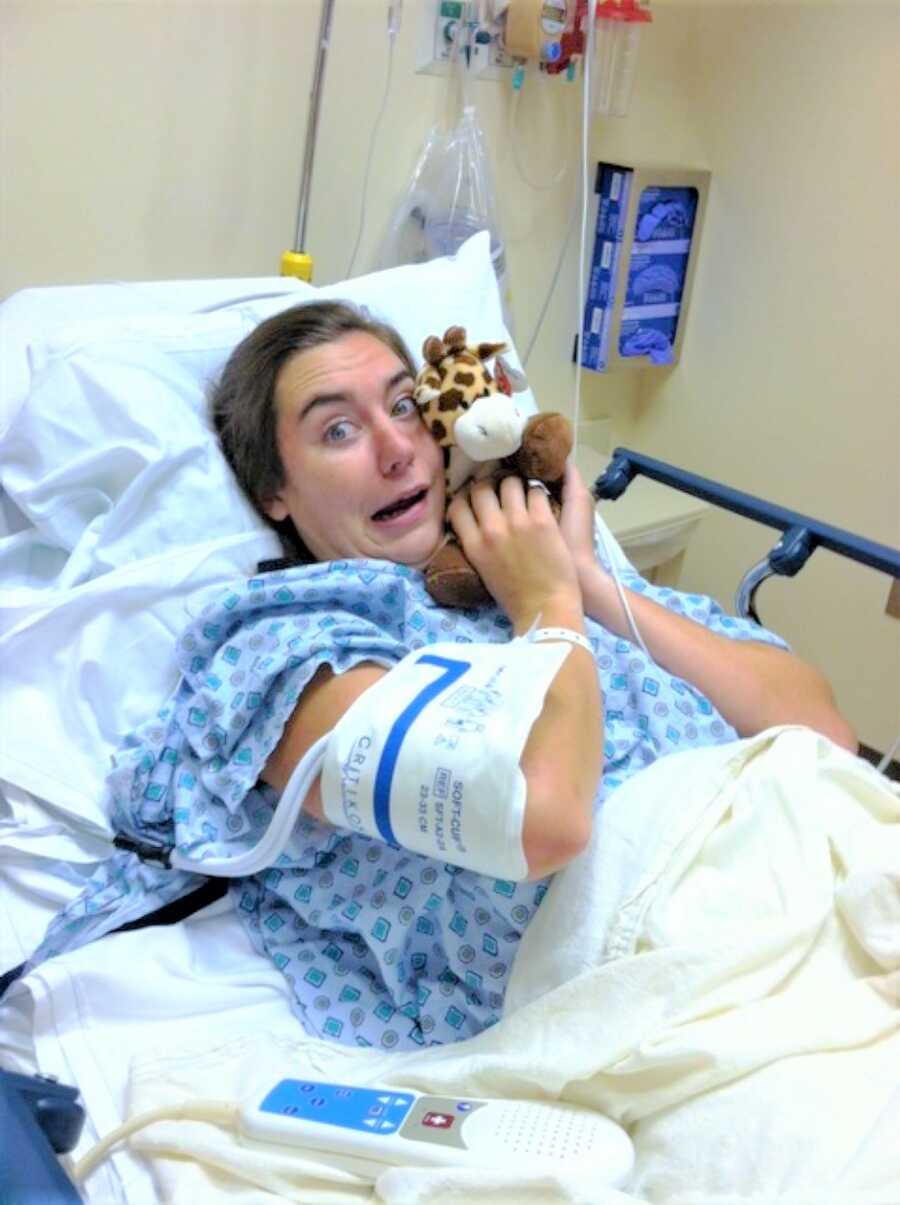 young woman looking nervous while laying in a hospital bed holding a stuffed giraffe before surgery 
