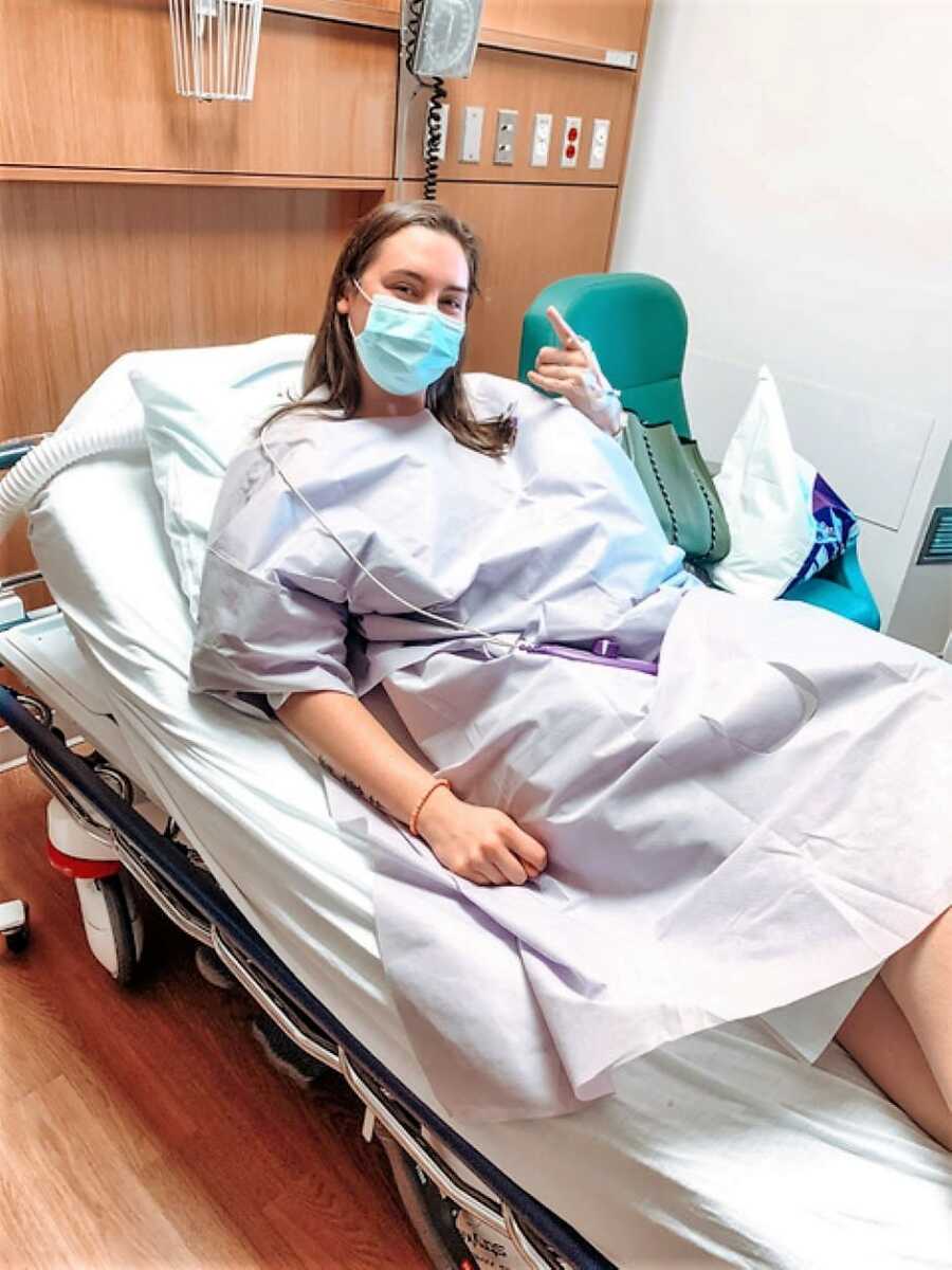 young woman in a hospital bed wearing hospital gown and mask before surgery 