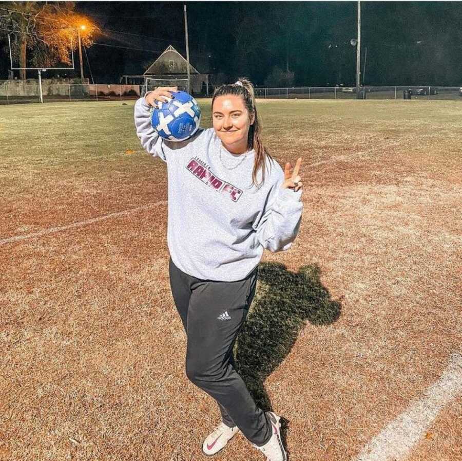 young woman in sportswear holding a soccer ball in a football field at night 