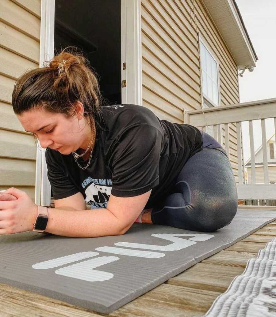 young woman doing stretches on a gray mat on a balcony 