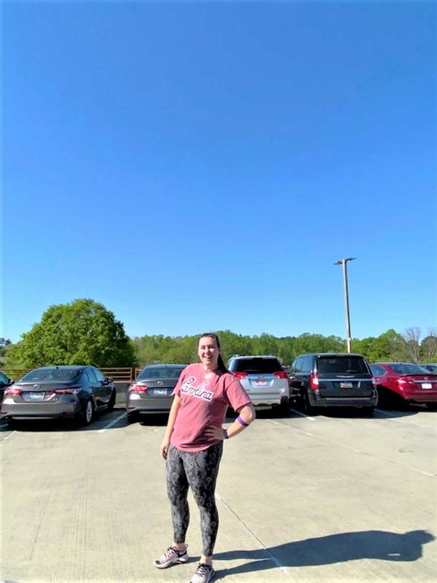 young woman standing on a parking lot wearing sportwear and smiling 