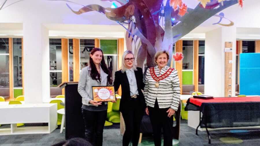 A woman holding a plaque and standing with two older ladies