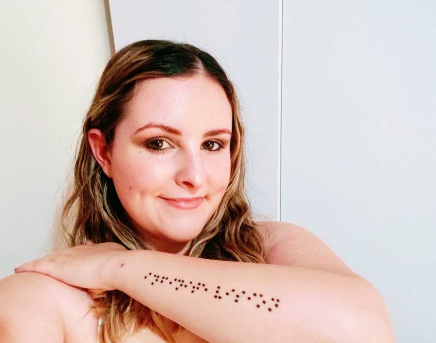 A visually impaired woman displays the Braille tattoo on her left forearm