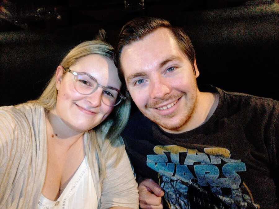 A woman wearing glasses and her fiance wearing a black T-shirt lean into each other
