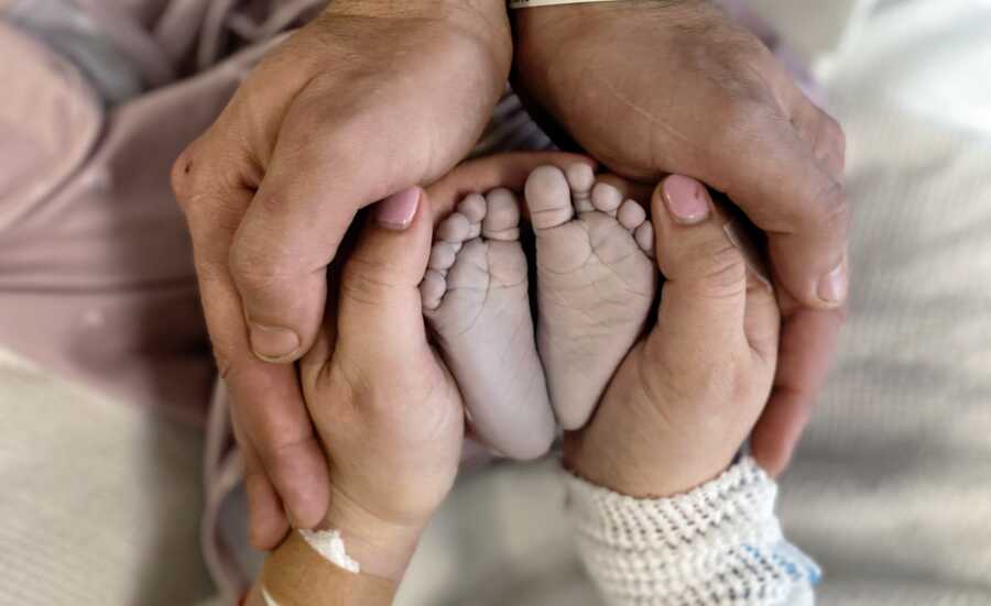 A mom and dad hold the feet of their stillborn baby girl