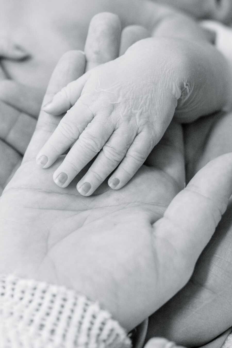 A baby's hand resting inside the hand of her mother