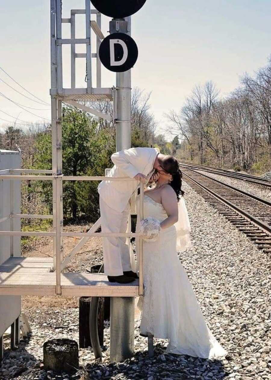 Husband and wife takes pictures in wedding clothes near railroad tracks.