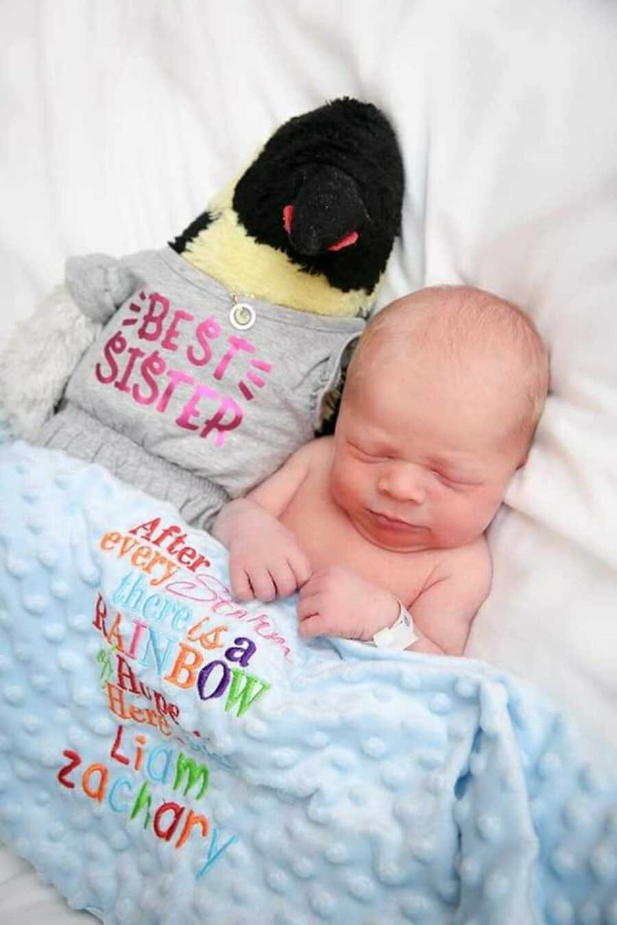 Rainbow baby brother takes picture next to sister's penguin.