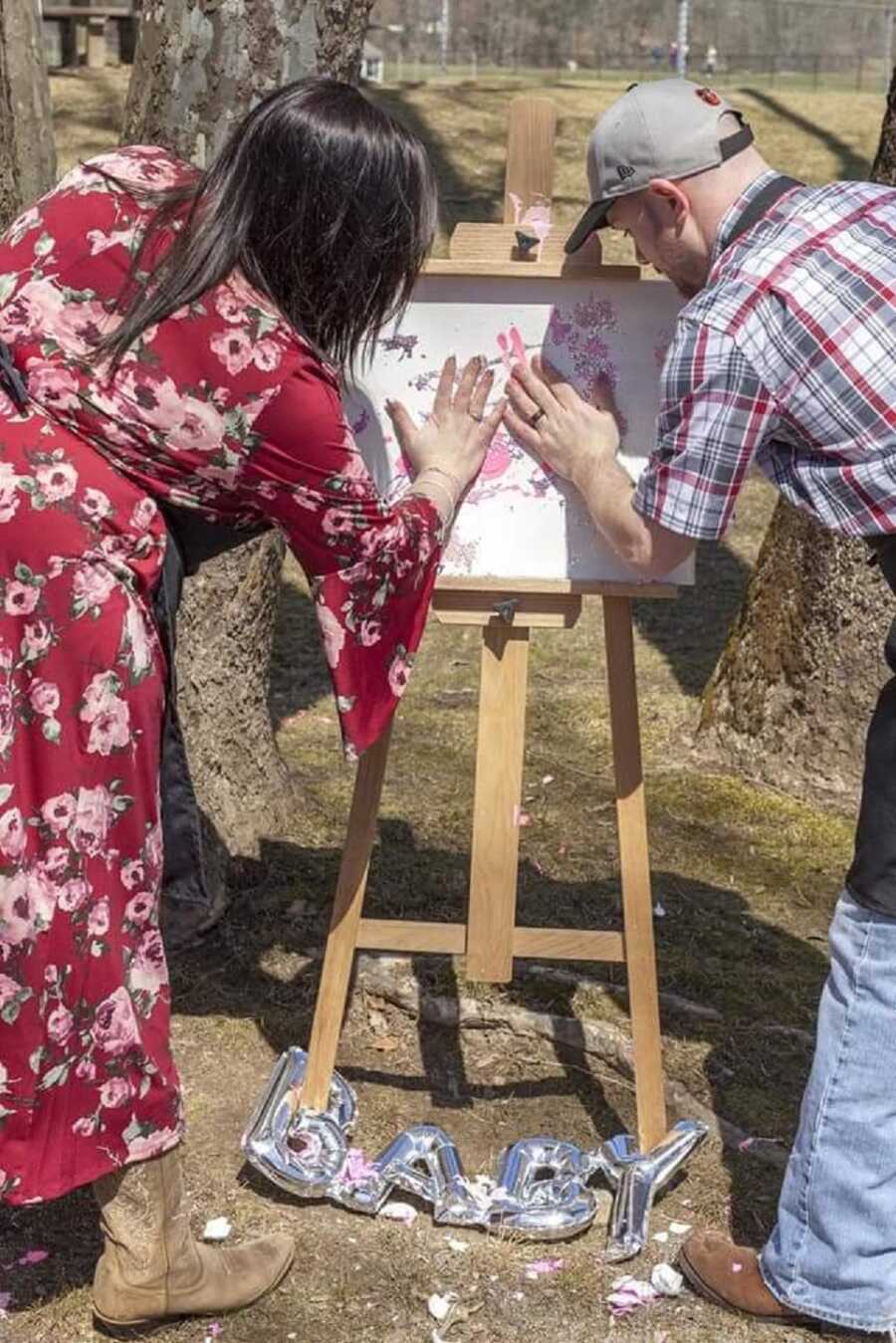 Couple paints canvas with pink paint from baby's gender reveal. 