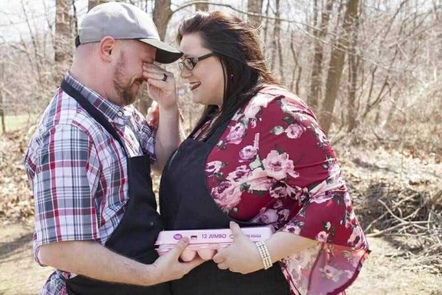 Husband and wife hold carton of Easter eggs for baby's gender reveal.