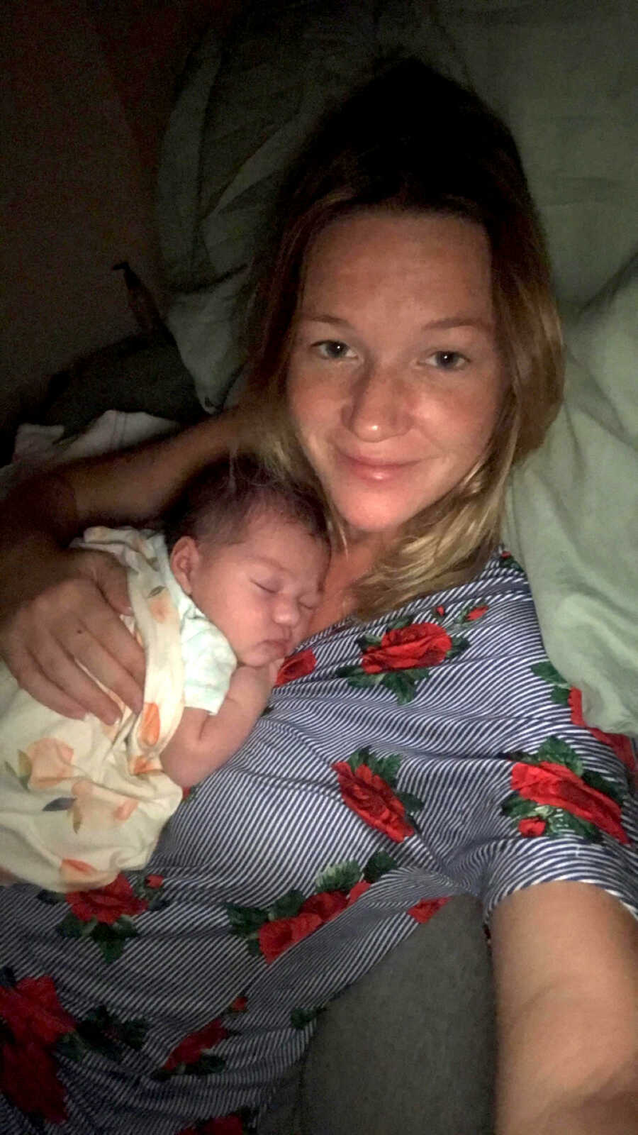 New mom holds baby against her chest and takes picture laying in bed. 