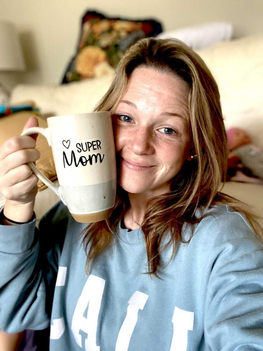 Woman holds up super mom coffee mug next to her face. 