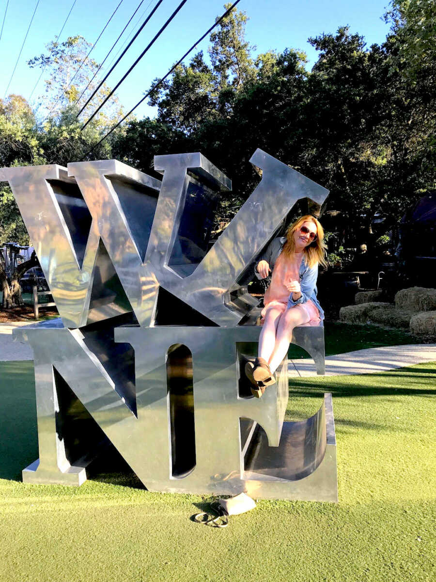 Woman sits on giant metal letters spelling wine.